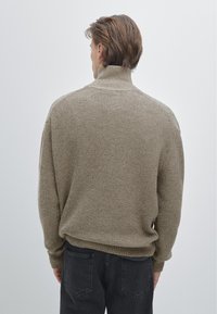 Béžový žebrovaný pletený svetr s vysokým límcem, s volným střihem a texturovaným povrchem, v kombinaci s černými džínami z denimu.