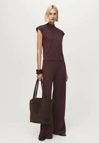 Burgundy knit top with cap sleeves paired with matching wide-leg pants. Model carries a dark brown suede tote bag. Smooth texture and relaxed fit.