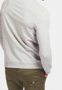 Szary sweatshirt z długimi rękawami, ściągaczami przy mankietach i u dołu. Nosi się go z oliwkowymi spodniami z tylnymi kieszeniami i logo marki na kieszeni.