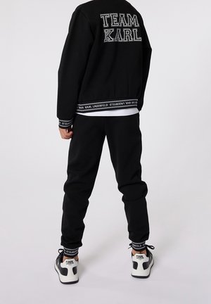 Person wearing black sweatpants and black sweatshirt with "TEAM KARL" text, paired with white and black Karl Lagerfeld sneakers.