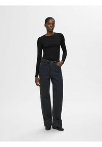 Sort langærmet top parret med mørkeblå brede bukser med høj talje og opsmøgede manchetter, båret med sorte slip-on sko.