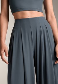 Donkergrijze geplooide wijde pijpen broeken gemaakt van een zachte, gladde stof. Kenmerkt zich door een hoge taille en een ontspannen pasvorm.