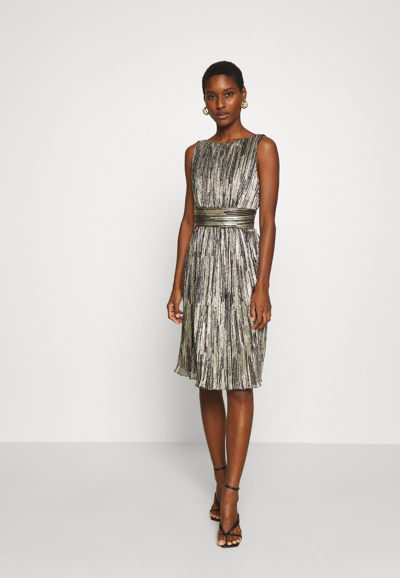 Robe plissée en tissu métallique argent et noir, dotée d'une taille et d'un design sans manches, longueur genou avec une silhouette fluide.