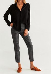 Chemise noire boutonnée, pantalon gris à motifs avec bandes latérales, et chaussures marron à enfiler. Tissu lisse et coupe ajustée.