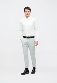 Weißes Hemd mit Knopfleiste und Brusttasche, graue maßgeschneiderte Hose und schwarze Lederschuhe, ergänzt durch einen schwarzen Gürtel. Glattes, minimalistisches Design.