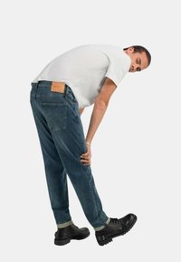 Jeans in denim blu scuro con taglio dritto, orlo risvolto e etichetta in pelle sul retro. Indossati con una maglietta bianca e stivali neri.