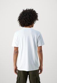 T-shirt bianco in cotone con maniche corte, colletto rotondo e vestibilità rilassata. Tessuto morbido, design semplice, cuciture visibili lungo le cuciture.