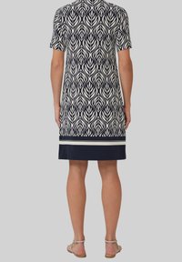 Kurzes Kleid mit einem Blattmuster in Marineblau und Creme. Verfügt über einen einfarbigen Marineblauen Saum mit zwei weißen Streifen am unteren Rand. Glatte Stofftextur.