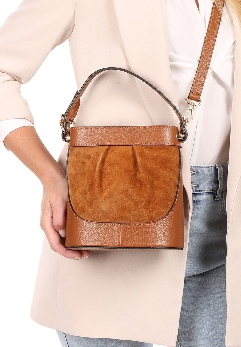 Braune Leder- und Wildleder-Eimer-Tasche mit einer vorderen Faltenoptik, kurzem Griff und abnehmbarem Gurt, ausgestattet mit einer strukturierten Oberfläche und glatten Akzenten.
