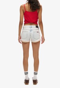 Lichtblauwe denim short met een geschulpte zoom en steekzakken aan de voorkant. Gecombineerd met een rood tanktop en bruine schoenen met witte en zwarte sokken.