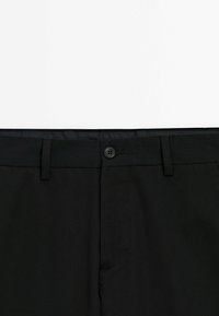 Pantalon noir habillé avec fermeture à boutons, passants de ceinture et devant plat sur fond blanc.