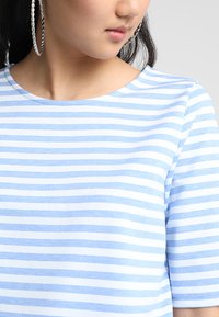 Lyseblå og hvid stribet kortærmet t-shirt med rund halsudskæring og glat tekstur, der har subtile stikninger.