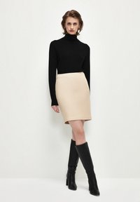 Svart polotröja, åtsittande krämfärgad kjol och knähöga svarta stövlar. Släta texturer och neutrala färger skapar en sammanhängande look.