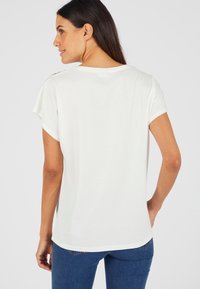 Witte t-shirt met korte mouwen van een gladde stof en een ronde halslijn, met decoratieve gouden hardware accenten op de schouder. Fitted design.