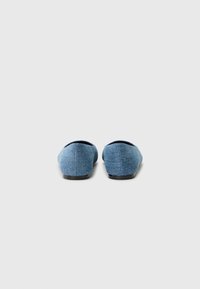 Denim slip-on shoes with a low profile, rounded toe, and black rubber sole. Textured blue fabric with a soft finish.
