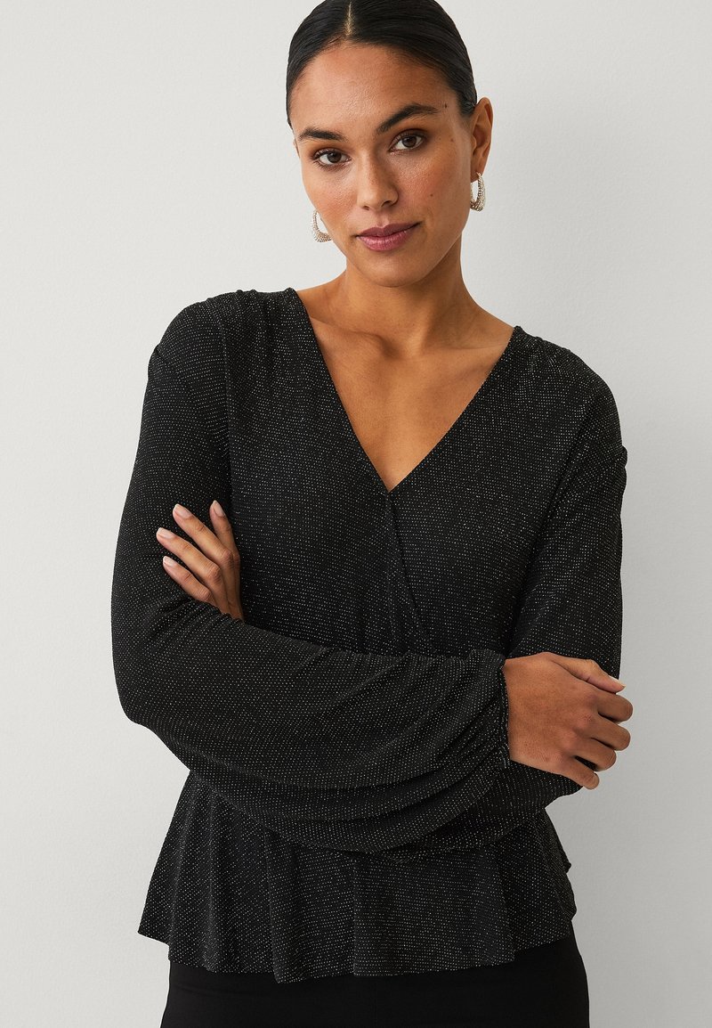 Schwarzes Oberteil mit V-Ausschnitt und langen, ausgestellten Ärmeln. Hergestellt aus glitzerndem Stoff mit einem Peplum-Saum, der ein strukturiertes Muster aufweist.