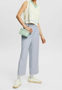 Osoba w kremowym bezrękawniku, jasnoniebieskich szerokich spodniach, białych trampkach z żółtymi akcentami, szarych skarpetach i nosząca miętową torbę na ramię.