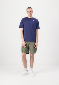 Navy blue short-sleeve t-shirt with a small logo, paired with green cargo shorts and white sneakers. Simple and functional design.