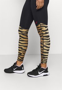 Czarne legginsy z beżowym nadrukiem tygrysa na dolnej części nóg, z czarnymi szwami. W zestawie z czarnymi sneakersami Nike z różowymi akcentami.