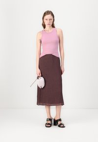 Helles rosa ärmelloses Oberteil, dunkelbraßer plissierter Maxirock, schwarze Sandalen mit Absatz und goldenen Akzenten sowie eine kleine graue Clutch.