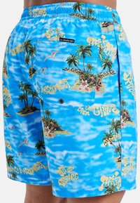 Modré plavkové šortky s tropickým vzorom zobrazujúcim palmy, ostrovy a obláčiky, doplnené žltým textom a zadnou vreckom.