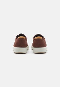 Chaussures en suède bordeaux avec des semelles en caoutchouc blanches, dotées d'un accent en cuir au talon et d'une forme arrondie, adaptées pour un usage décontracté.