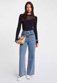 Un haut noir à manches longues en maille côtelée avec un empiècement en filet rayé, associé à un jean en denim bleu à jambes larges et un petit sac tissé. Baskets blanches.