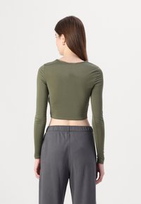 Olive green, long-sleeved cropped top in a fitted design, paired with loose-fitting gray pants featuring an elastic waistband.