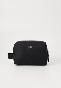 Svart, rektangulær toalettmappe laget av slitesterk stoff, med glidelås-lukking, et sidelokket og GANT-logoen på forsiden.