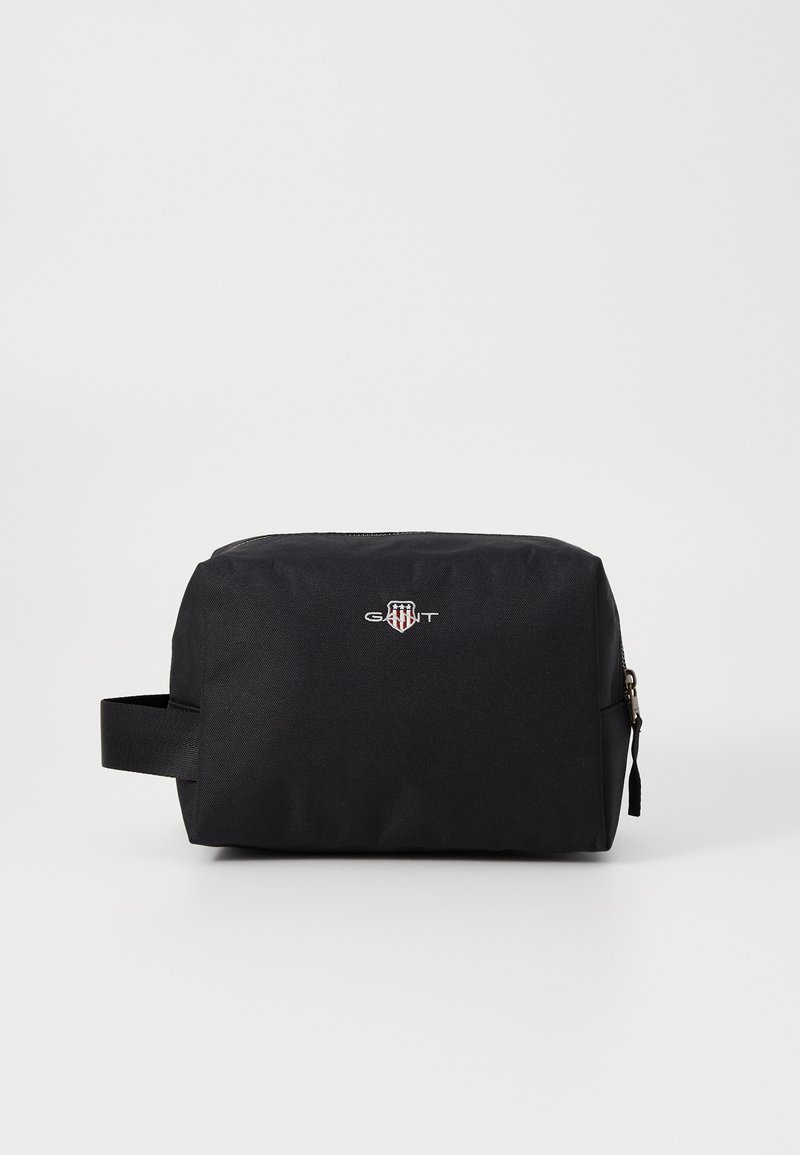 Svart, rektangulær toalettmappe laget av slitesterk stoff, med glidelås-lukking, et sidelokket og GANT-logoen på forsiden.