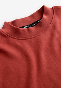 Bordeauxfarbenes Sweatshirt mit ribbeligem Rundhalsausschnitt, weicher Textur und gestickten Details. Das Etikett im Kragen trägt die Aufschrift "Ted Baker".