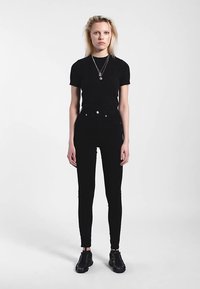 Musta istuva lyhythihainen t-paita, yhdistetty korkeavyötäröisiin mustiin kapealahkeisiin farkkuihin. Mallilla on mustat jalkineet ja kerroksittain hopeisia kaulakoruja.