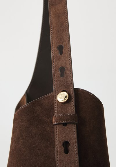Sac en daim marron avec un corps arrondi, une longue bandoulière réglable avec des accents en forme de clé, et un détail de fermeture à bouton doré.