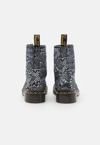 Botines de tobillo con estampado de serpiente en blanco y negro, con textura suave, costuras amarillas, suela gruesa y una lazada en la parte superior para facilitar su uso.