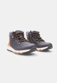 Scarpe da trekking blu navy e beige realizzate in materiali mesh e pelle, con dettagli arancioni, superfici texture e un design della suola a zigzag.