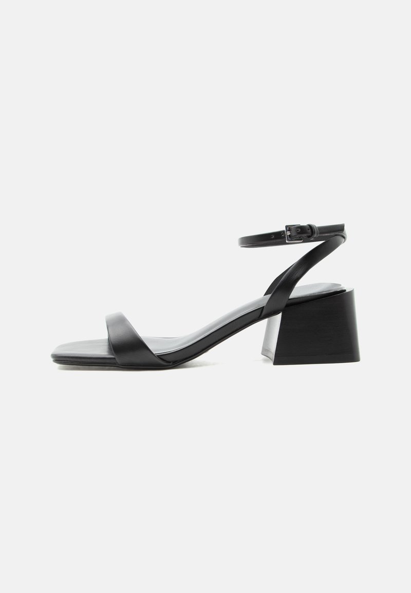 Sandale noire en cuir à bout ouvert, talon bloc, fine bride à la cheville et fermeture à boucle, vue de profil sur fond blanc.