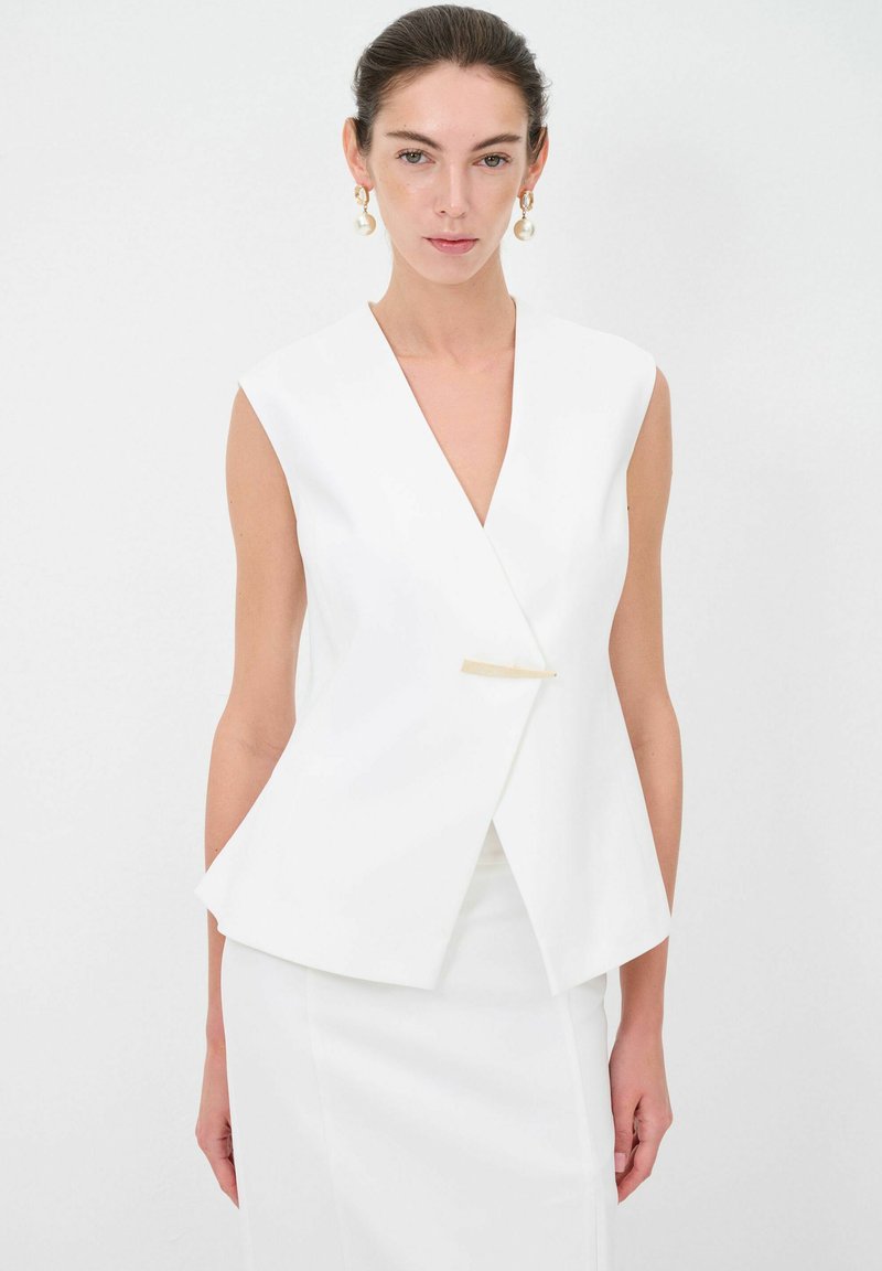 Witte mouwloze blazer met een diepe V-hals, gestructureerd ontwerp en gouden sluiting. Gladde textuur, op maat gemaakt pasvorm, minimalistische esthetiek.