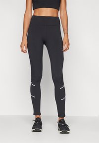 Leggings de sport noirs avec une taille haute et des bandes réfléchissantes blanches sur les côtés, fabriqués en tissu extensible et évacuant l'humidité.