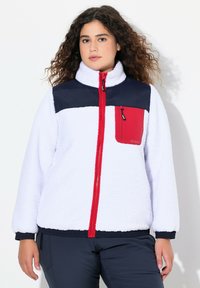 Veste en polaire avec un corps blanc, des épaules bleu marine et une fermeture éclair rouge ainsi qu'une poche. Elle possède une fermeture éclair à l'avant et un tissu texturé.