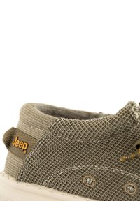 Sneaker in tela verde oliva con superficie texturizzata, suola in gomma bianca e logo giallo della Jeep. Presenta cuciture e fori di ventilazione laterali.