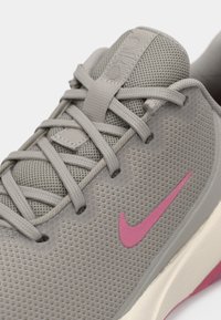 Graue Netzsportchuhe mit pinkem Nike-Swoosh, grauen Schnürsenkeln und gepolstertem Zungenbereich mit eingeprägtem Branding.