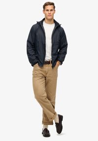 Navy windbreaker with a hood, elastic cuffs, and zipper front. Paired with khaki pants and dark loafers. Simple white t-shirt underneath.