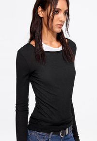 Black long-sleeve top with a round neckline, featuring a soft texture and fitted design, layered over a white underlayer.