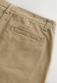 Bežīgas kokvilnas bikses ar taisnu griezumu, ar aizmugurējo kabatu un smalku diagonālu svītru tekstūru, šūtiem jostasvītnēm un jostas cilpām.