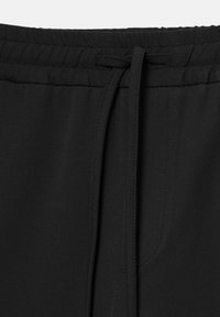 Zwarte stof drawstring tailleband met een gestrikt strikje en zichtbare stiksels op casual broeken of shorts.