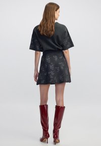 Grijs shirt met korte mouwen en een getailleerde taille, gecombineerd met een uitlopende rok met een subtiel bloemenpatroon en glanzende rode kniehoge laarzen.