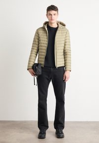 Obložena olivno zelena jakna s zadrgo, črna majica, črne kavbojke in črne superge. Mala črna torba z vrvico v roki.