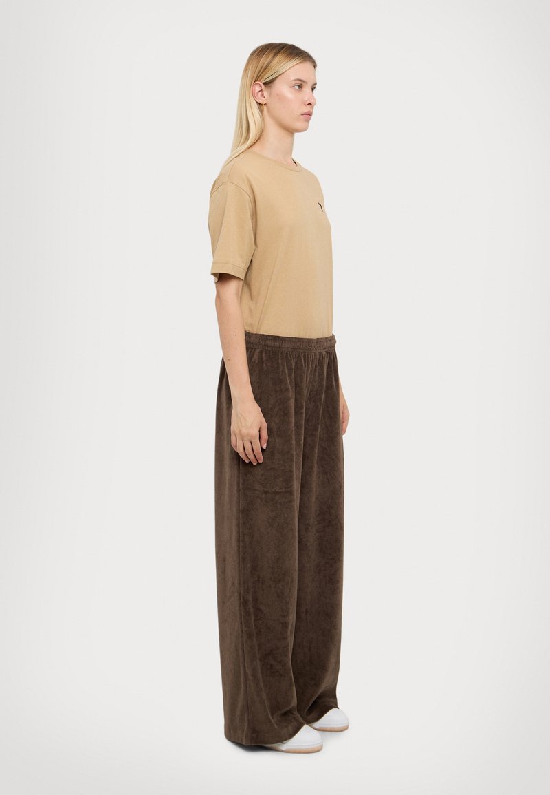 Lichtbruine t-shirt met korte mouwen en bruin fluwelige brede broek. De t-shirt heeft een klein logo; de broek heeft een elastische tailleband en een gladde textuur.