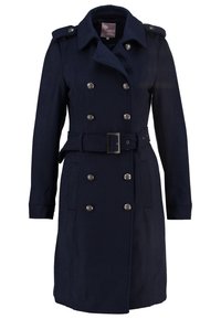 Marinblå dubbelknäppt kappa gjord av mjukt tyg, med silverfärgade knappar, bälte i midjan och axelklaffar. Långa ärmar och rak skärning.