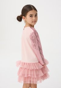 Abito rosa con top aderente e maniche con paillettes, e una gonna a ruota a strati con volant in morbido tulle. Texture liscia, colore vivace.